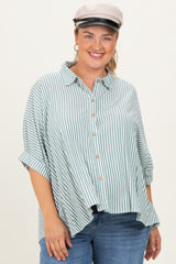 woman wearing a green and white striped maternity plus button-up shirt with rolled sleeves and a playful smile