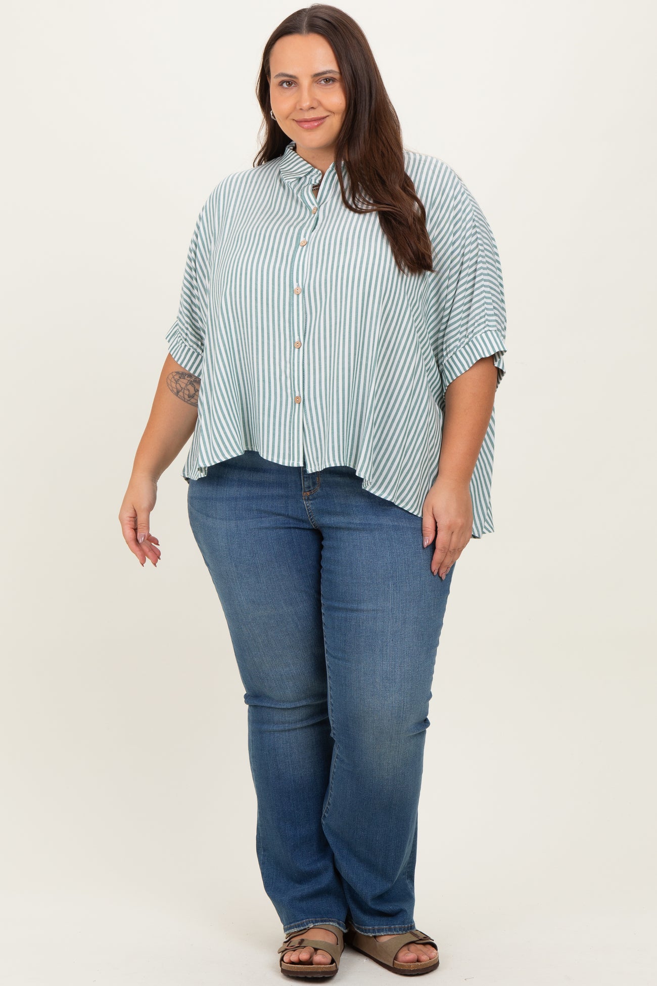 woman wearing a light green and white striped button-up shirt with rolled sleeves and blue jeans