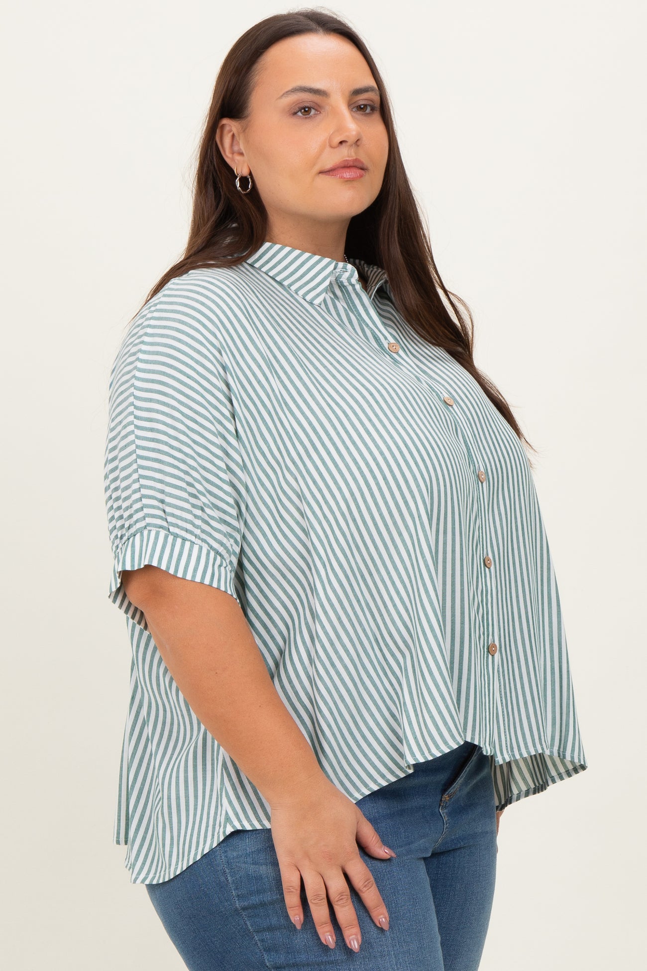 plus size woman wearing a green and white striped button-up shirt with short sleeves and a side slit, paired with blue jeans