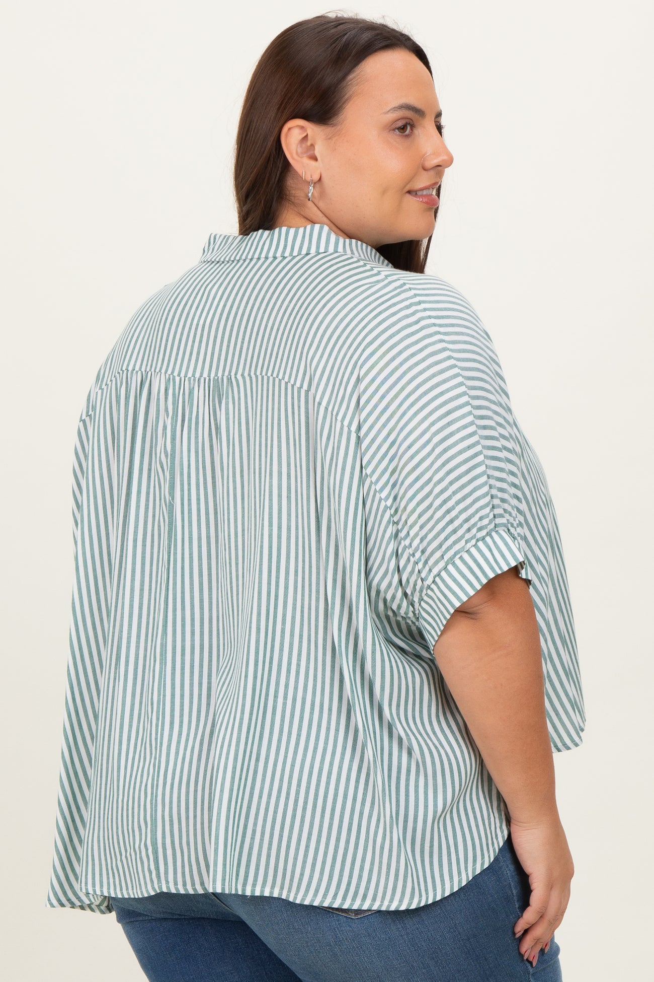 plus size woman wearing a light green and white striped oversized shirt with a back pleat and rolled sleeves