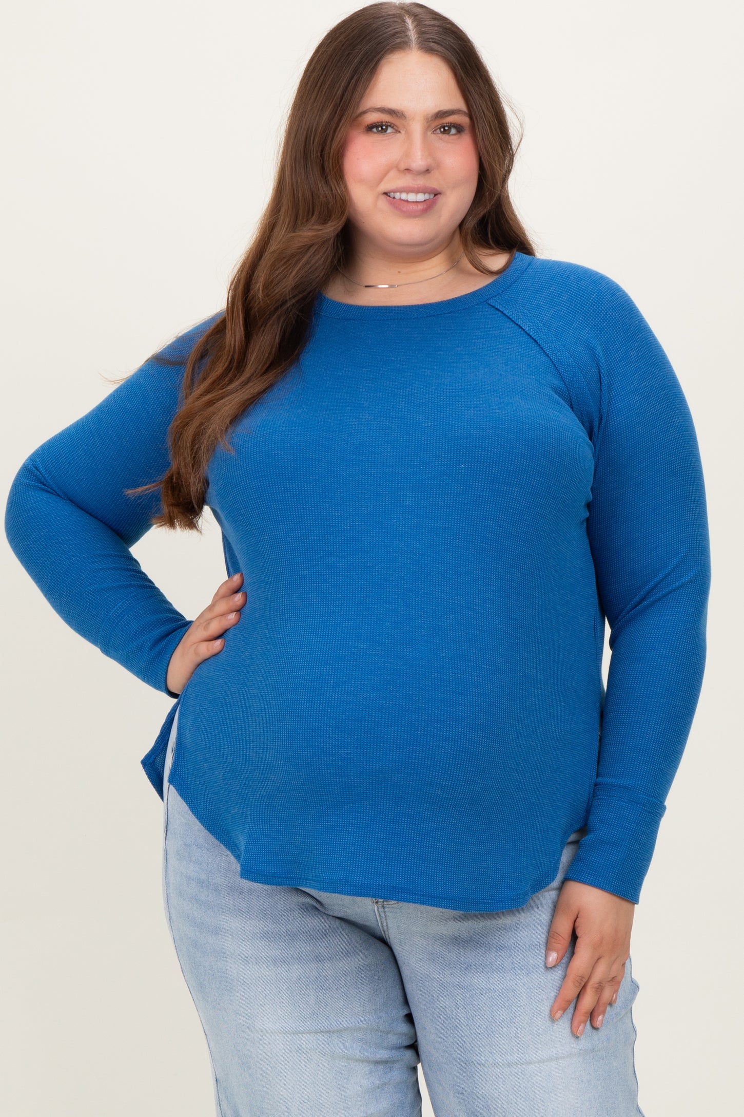 woman wearing a bright blue long sleeve maternity plus top with side slits and a relaxed fit
