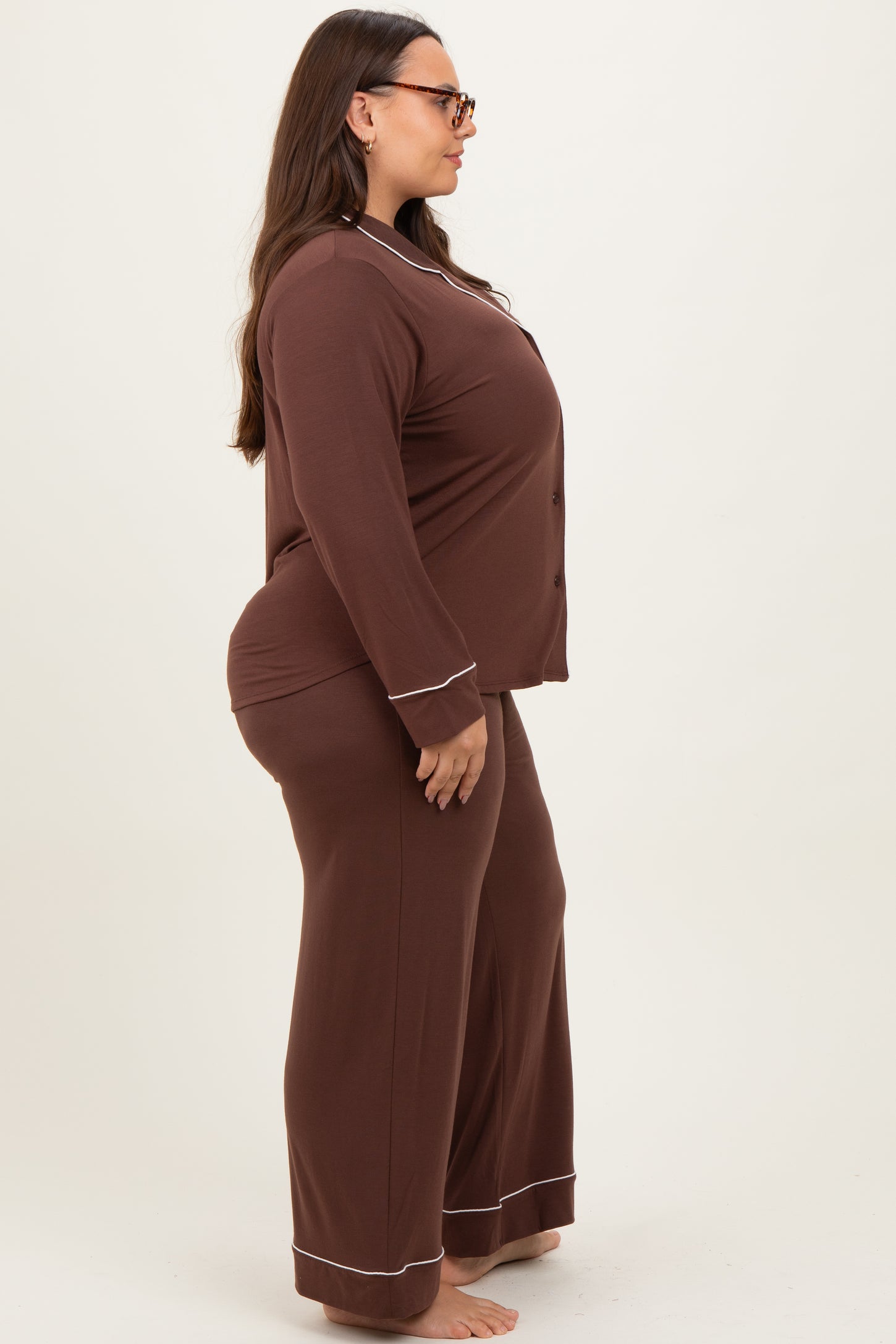 woman wearing a brown long sleeve plus size pajamas set with contrasting white piping, standing sideways