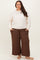 woman wearing a cream oversized sweatshirt and brown wide-leg pants, standing barefoot with hands in pockets