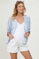 woman wearing a light blue button-up maternity shirt over a white tank top and white shorts, showing her baby bump