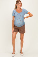 woman wearing a blue floral short sleeve maternity top and brown shorts, showing her baby bump