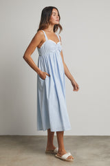 woman wearing a light blue midi dress with a gathered bodice and lace trim, featuring side pockets and wearing sandals