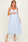 woman wearing a light blue striped maternity dress with adjustable straps and a gathered waist, holding her baby bump