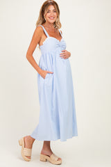 woman wearing a light blue striped maternity dress with pockets and adjustable straps, holding her baby bump