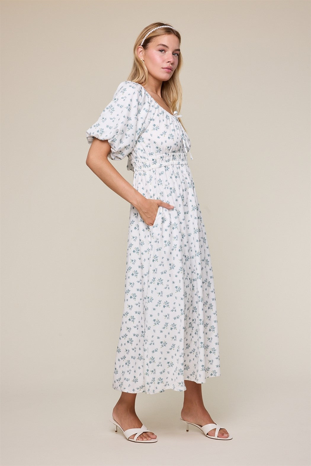 woman wearing a white floral midi dress with puff sleeves and pockets, standing in profile