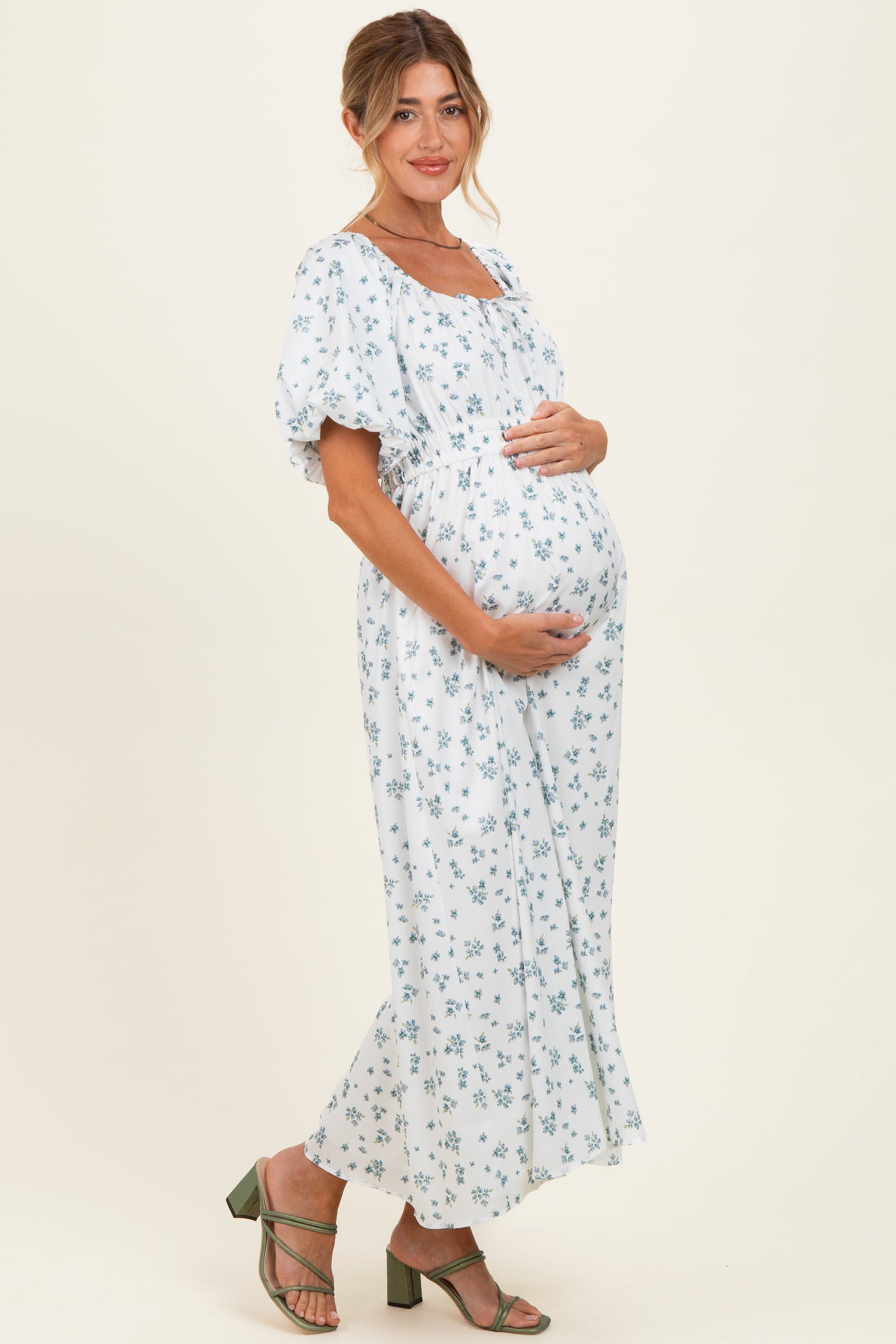 woman wearing a light blue floral maternity dress, holding her baby bump, with puffed sleeves and a flowy skirt