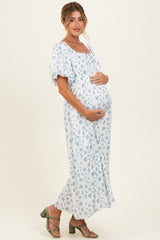 woman wearing a light blue floral maternity dress, holding her baby bump, with puffed sleeves and a flowy skirt