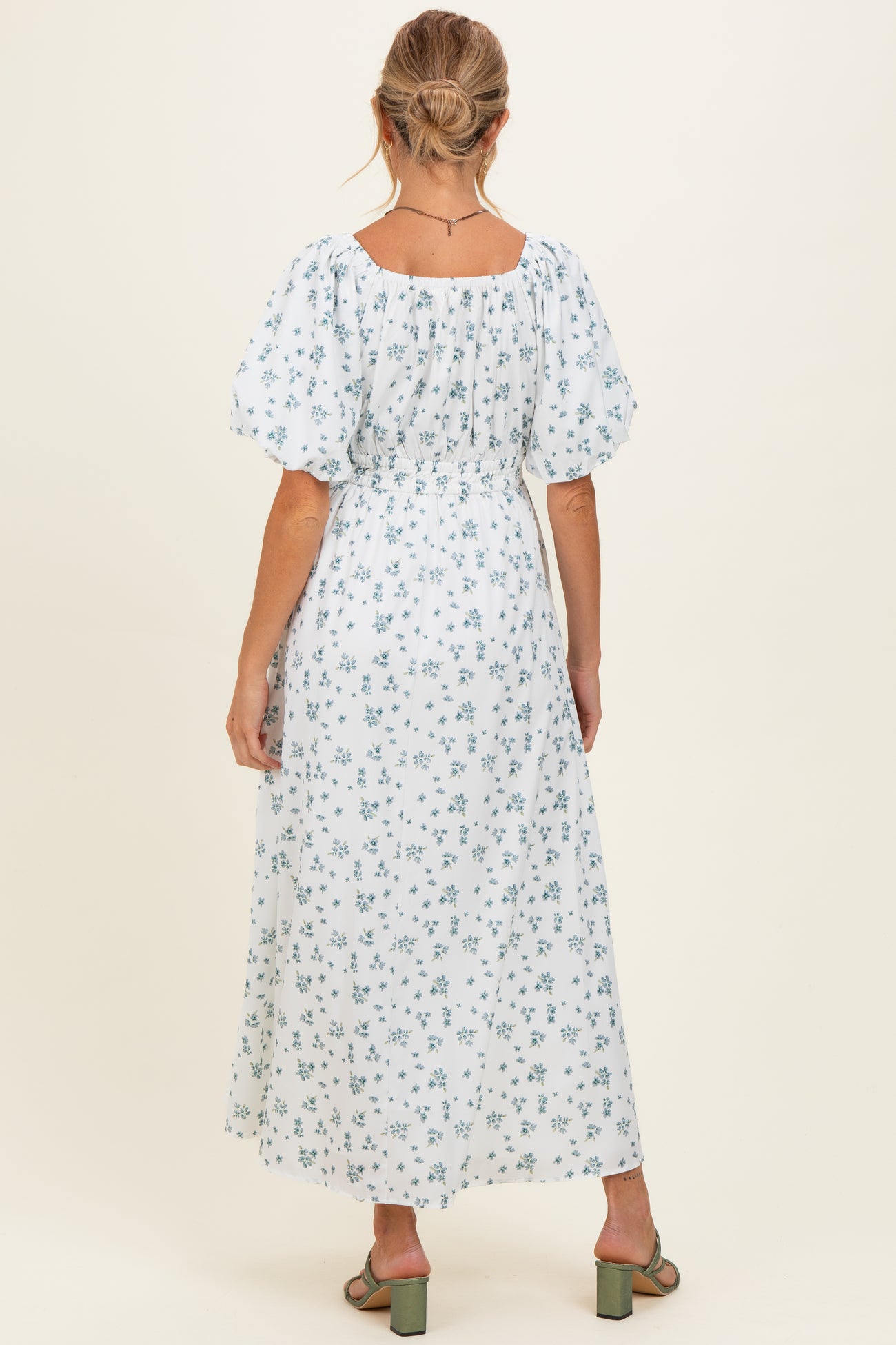 woman wearing a white floral maternity maxi dress with puff sleeves and a cinched waist, showing her back