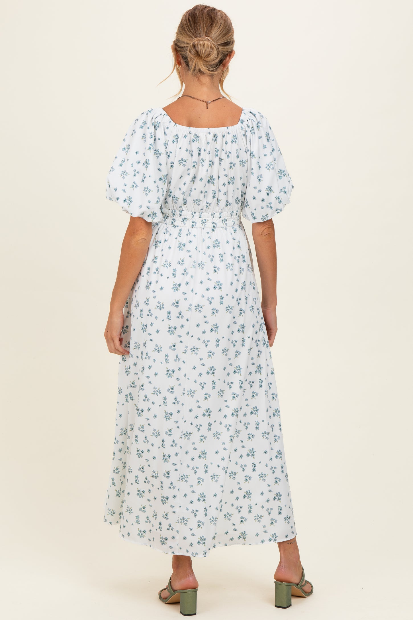 woman wearing a white floral maternity maxi dress with puff sleeves and a cinched waist, showing her back