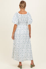 woman wearing a white floral maternity maxi dress with puff sleeves and a cinched waist, showing her back