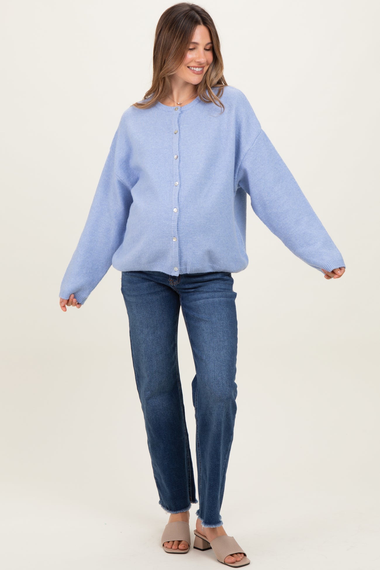 woman wearing a light blue oversized maternity cardigan with buttons, styled with blue jeans and heeled sandals