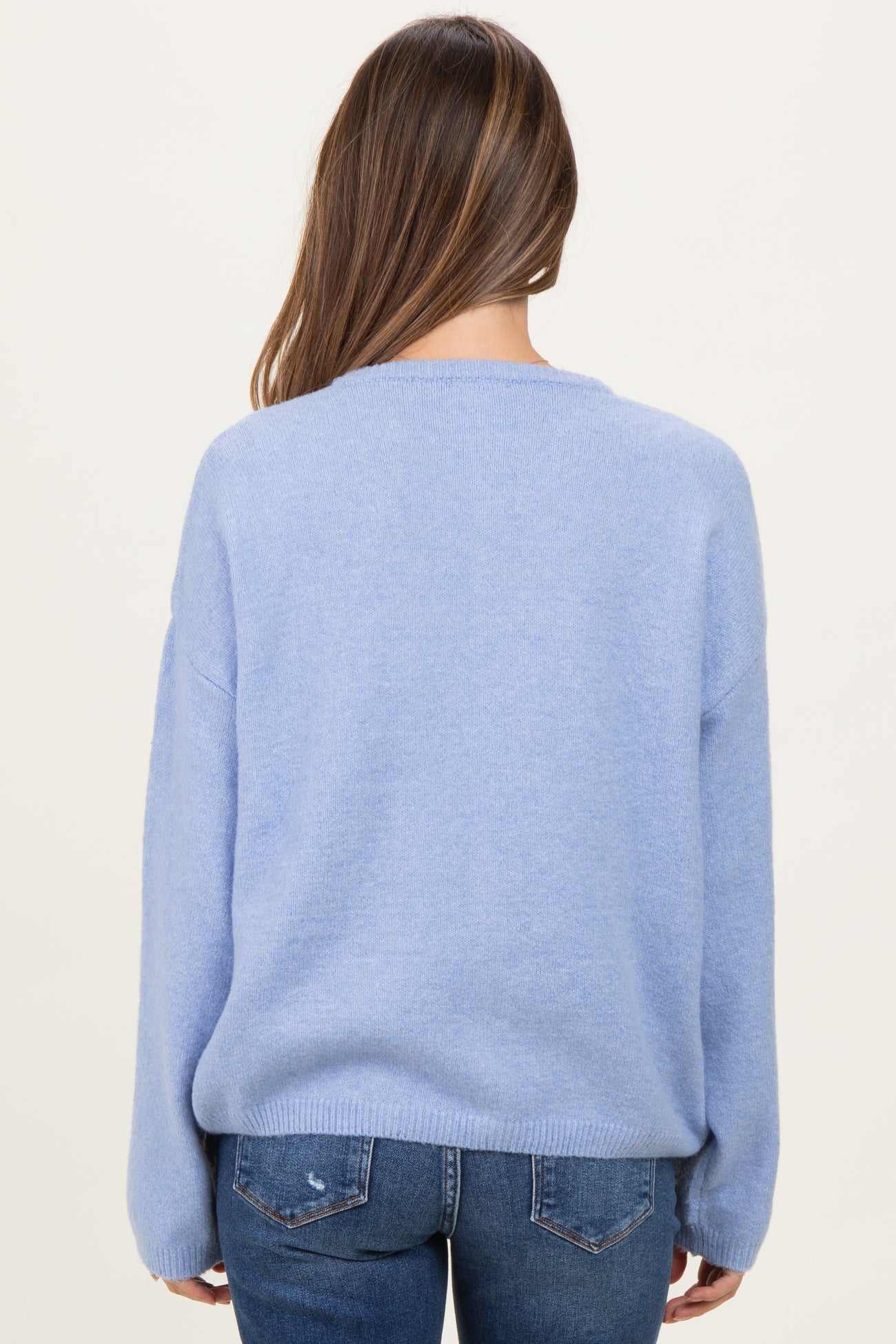 woman wearing a light blue oversized maternity sweater, seen from the back, paired with dark jeans