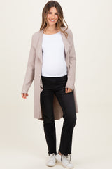 woman wearing a light pink maternity long cardigan over a white top and black jeans, showing her baby bump