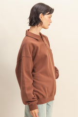 woman wearing a brown oversized polo sweatshirt with a collar and side pockets