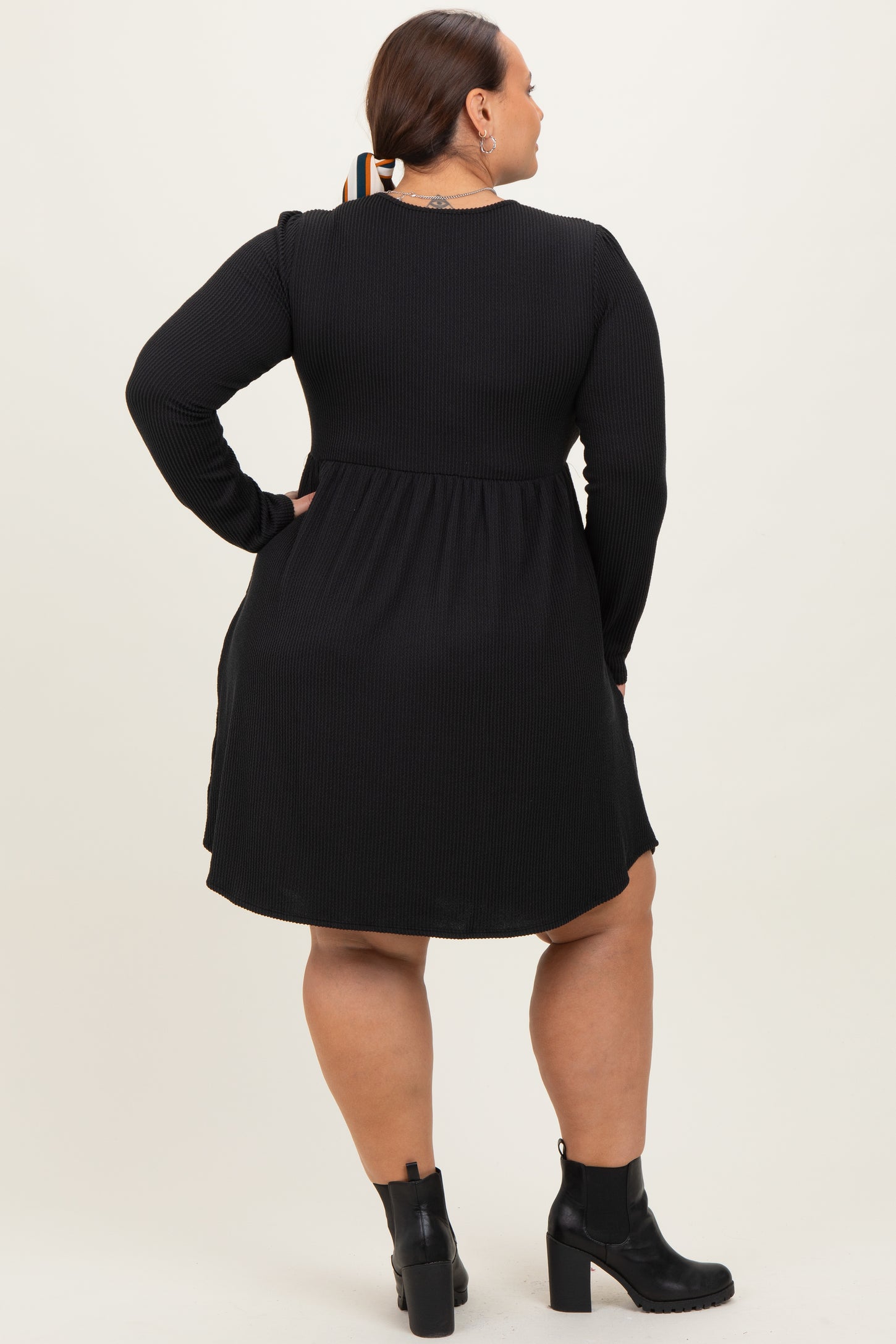 woman wearing a black long sleeve plus size dress with a flared skirt and ankle boots, viewed from the back