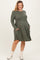 woman wearing an olive green long sleeve maternity dress with pockets and a visible baby bump