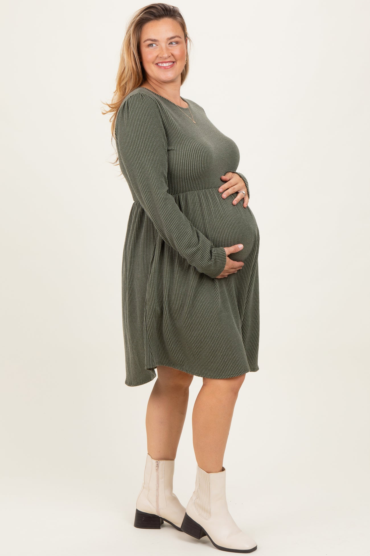 woman wearing a green ribbed long sleeve maternity dress and holding her baby bump