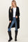 woman wearing a black long coat over a white top and blue jeans, paired with black knee-high boots