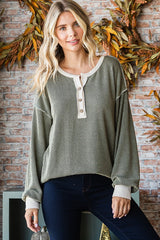 woman wearing an olive green oversized knit sweater with button details, styled with dark jeans and a casual look