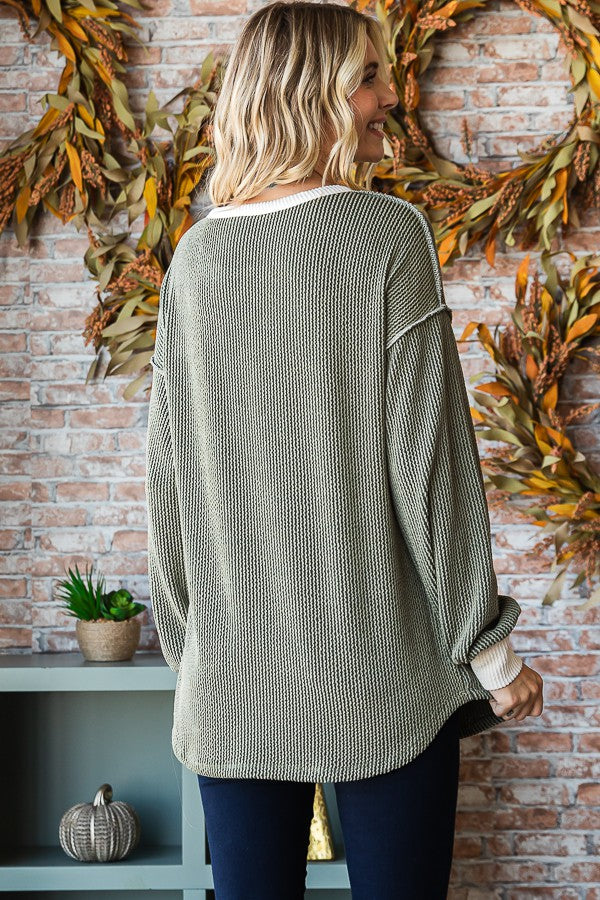 woman wearing a green oversized knit sweater with white trim, viewed from the back against a brick wall