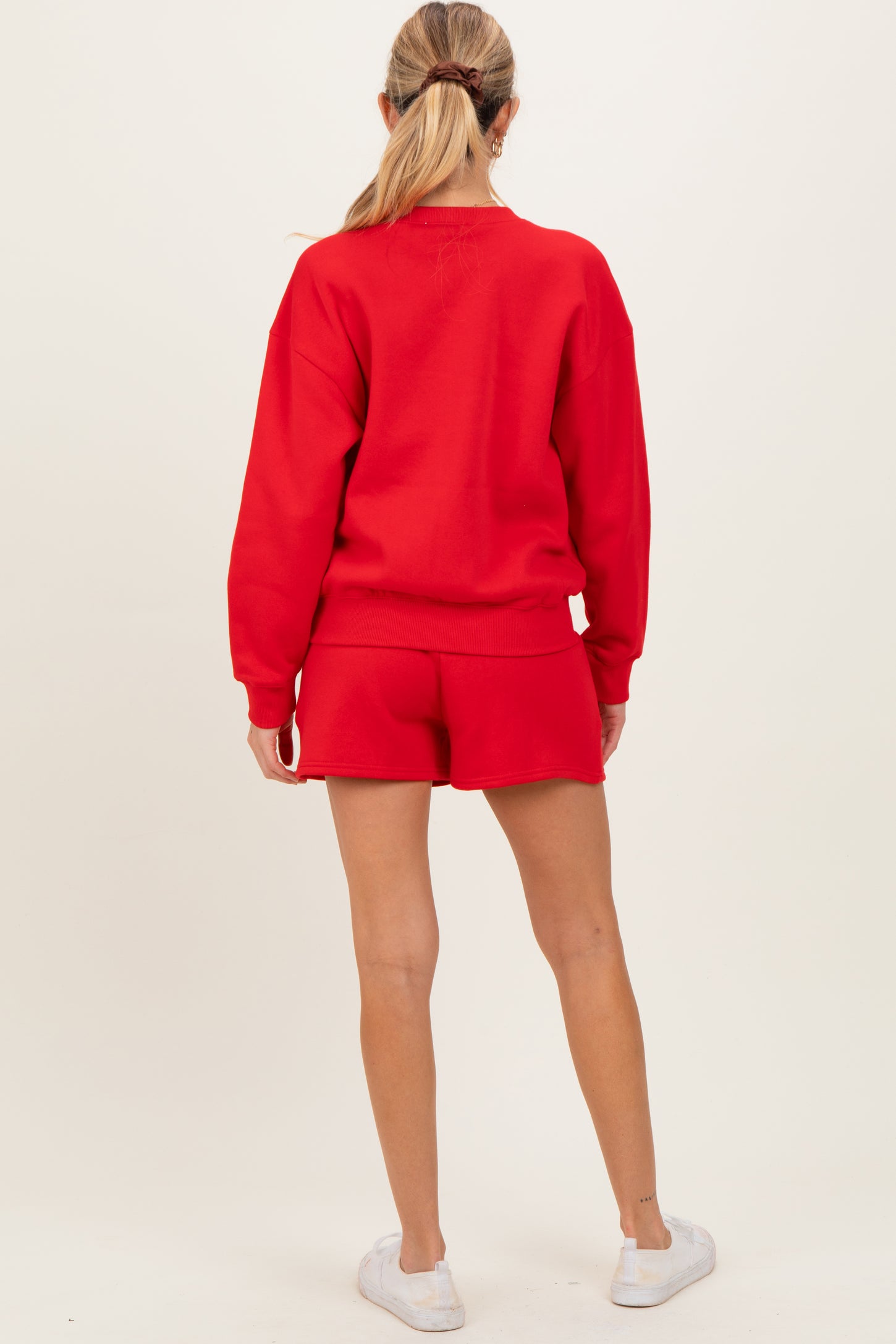 woman wearing a red maternity sweatshirt and matching shorts, showing a discreet baby bump from the back