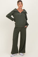 woman wearing an olive green maternity zip-up sweater and matching wide-leg pants