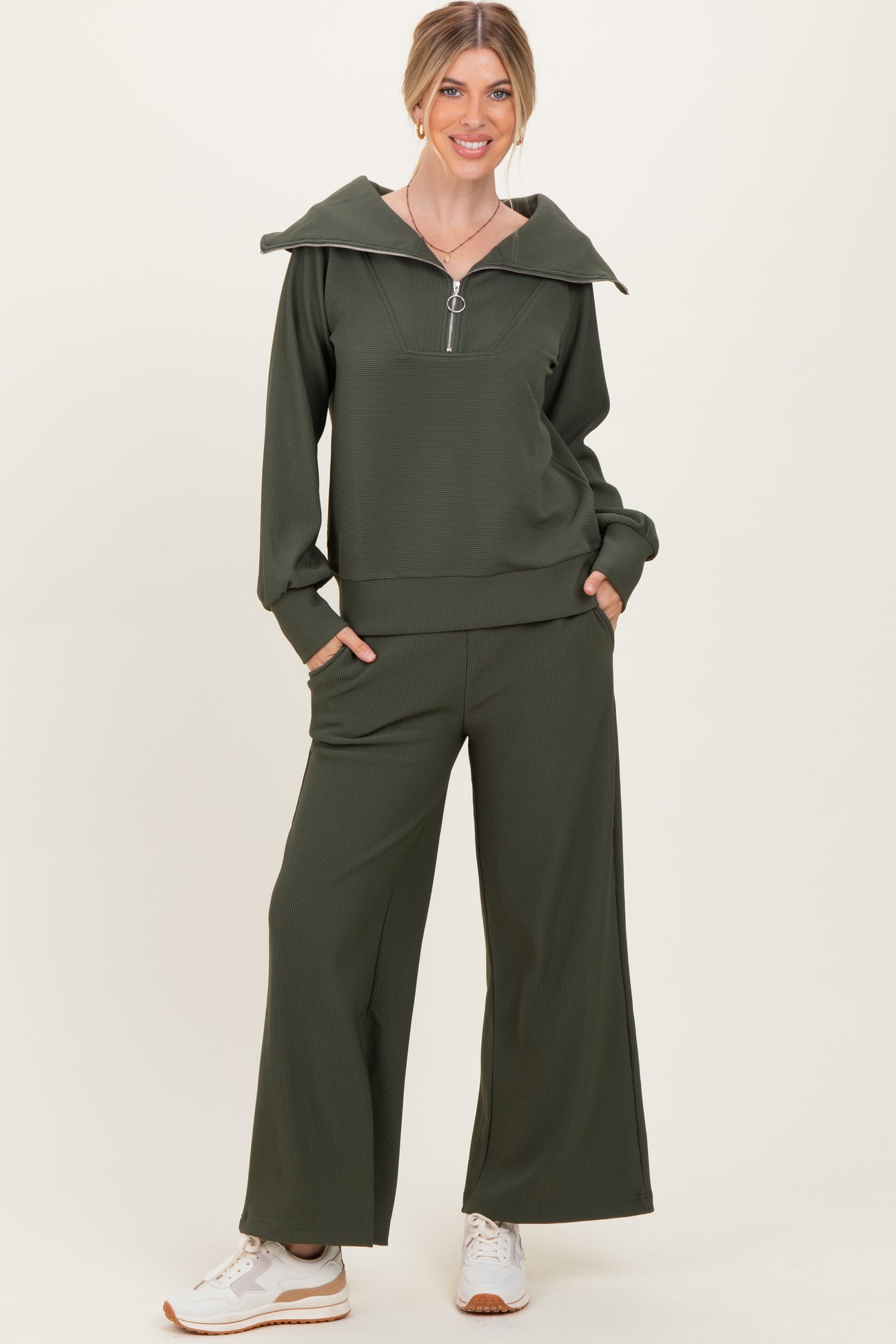 woman wearing an olive green zip-up hoodie with an oversized collar and matching wide-leg pants, styled with white sneakers
