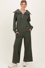 woman wearing an olive green zip-up hoodie with an oversized collar and matching wide-leg pants, styled with white sneakers