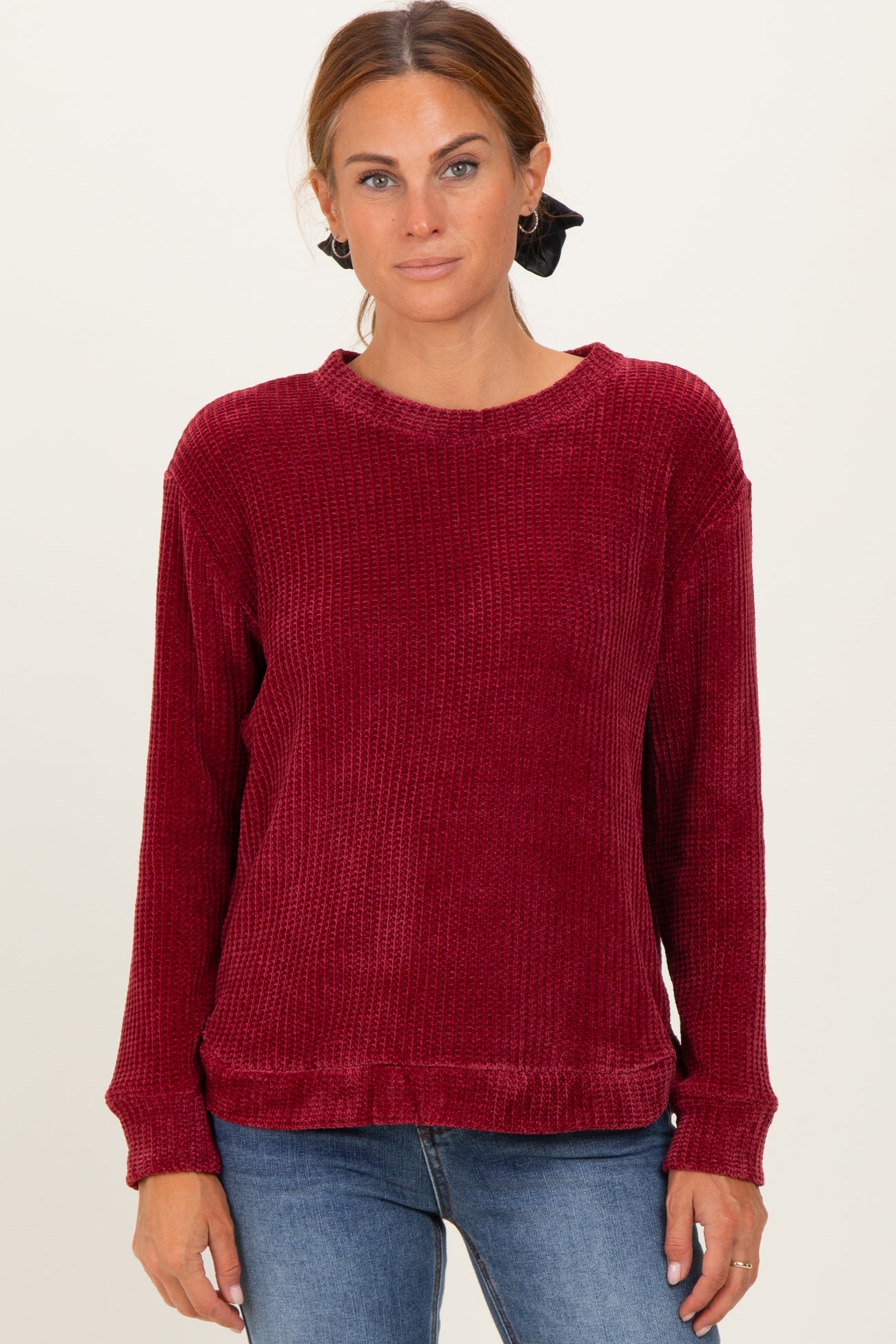 woman wearing a burgundy fuzzy long sleeve sweater with ribbed texture and relaxed fit, styled with blue jeans