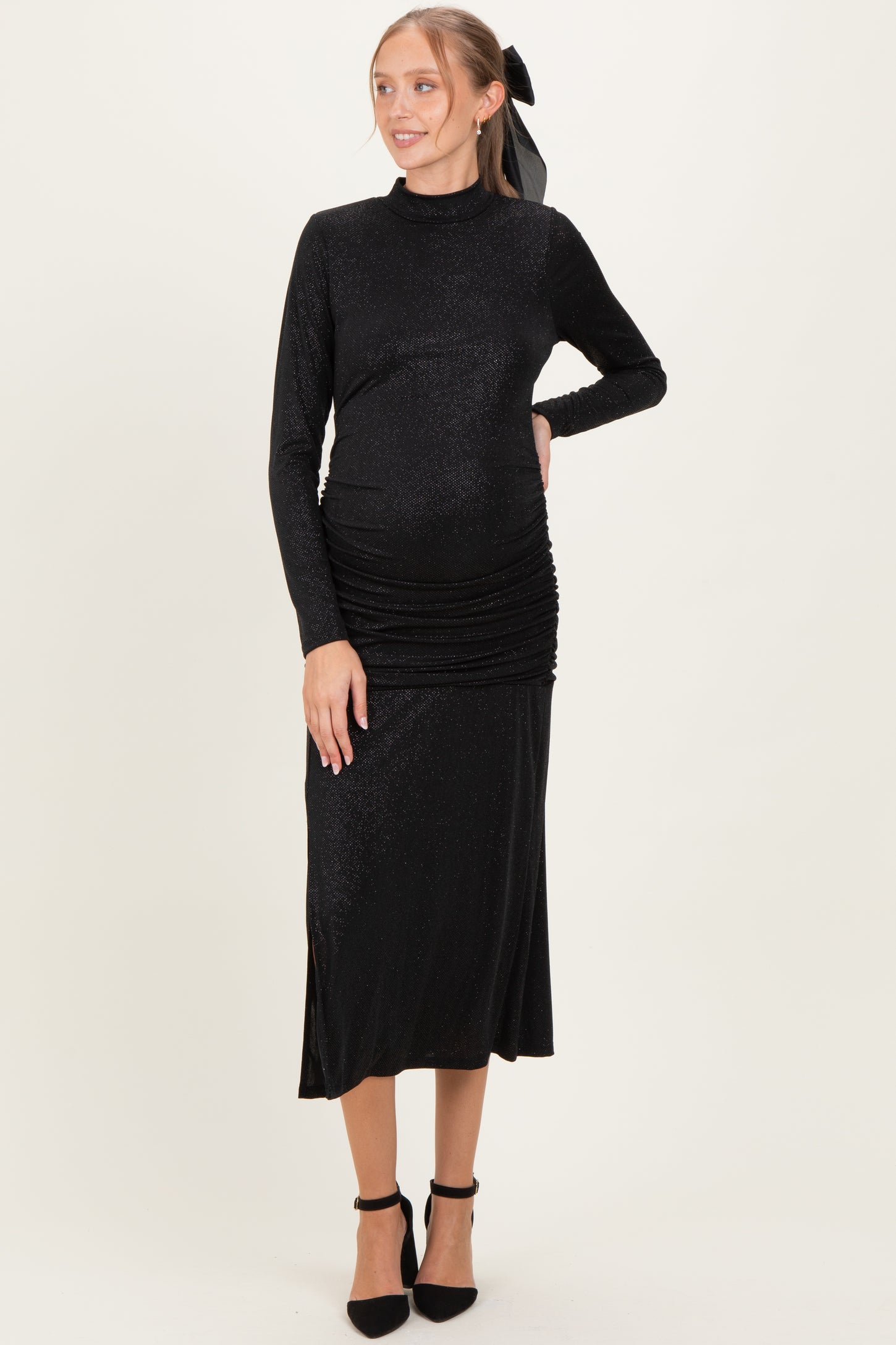woman wearing a black long sleeve maternity dress with side ruching and a high neckline, showcasing her baby bump