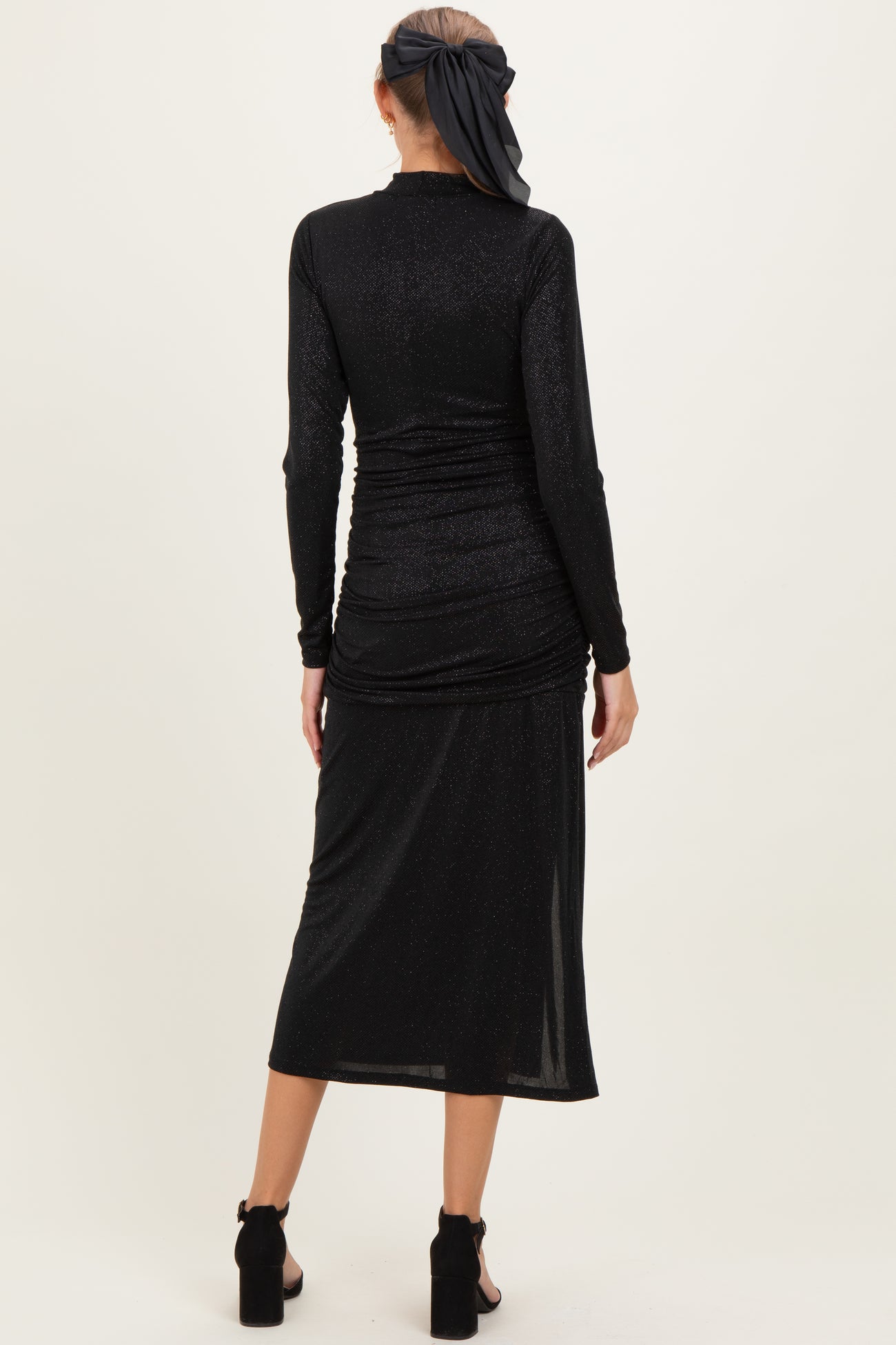 woman wearing a black long sleeve maternity dress with ruched detailing and a midi length, styled with a headscarf