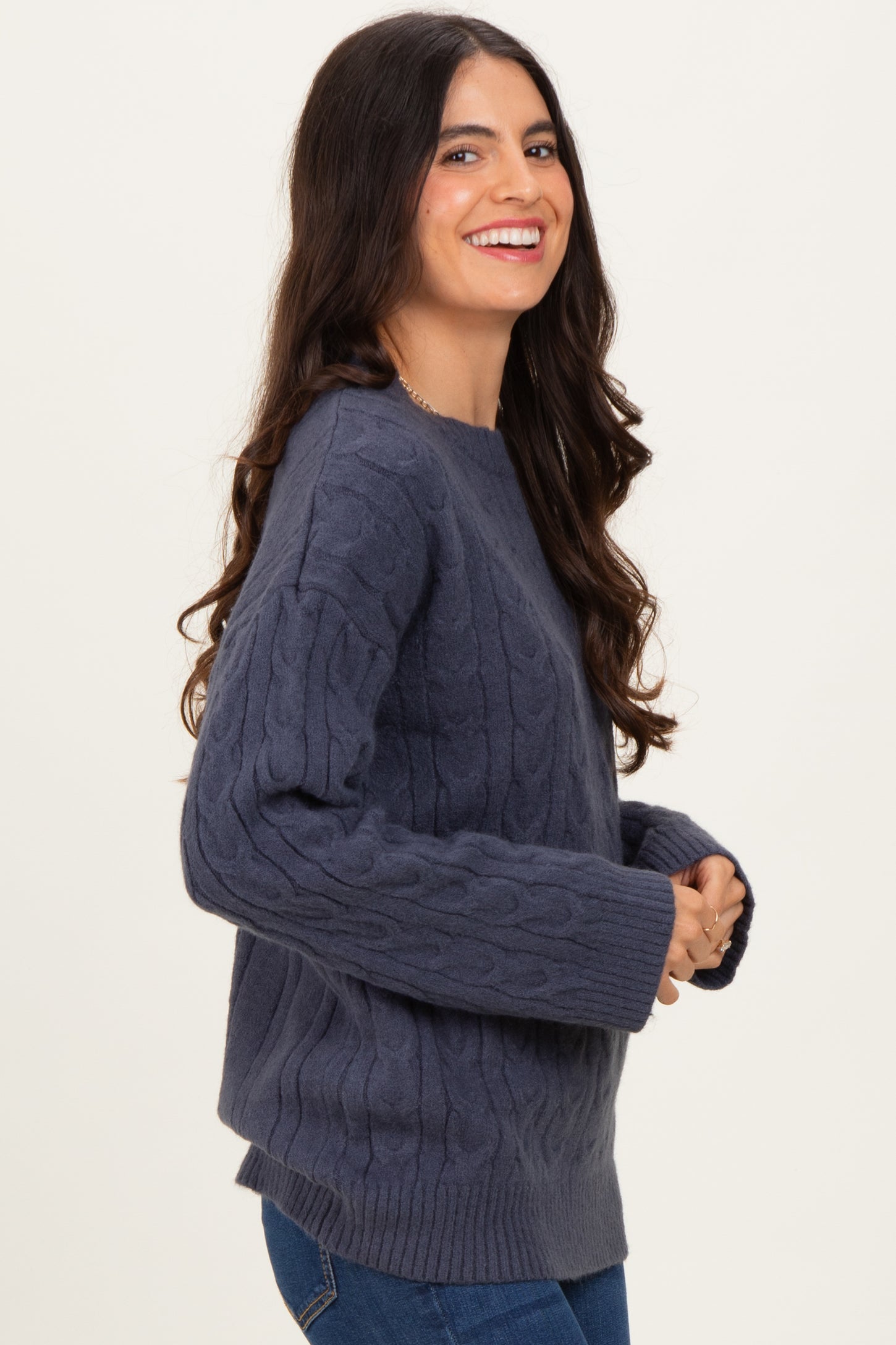woman wearing a dark grey cable knit sweater with a relaxed fit and long sleeves, smiling at the camera