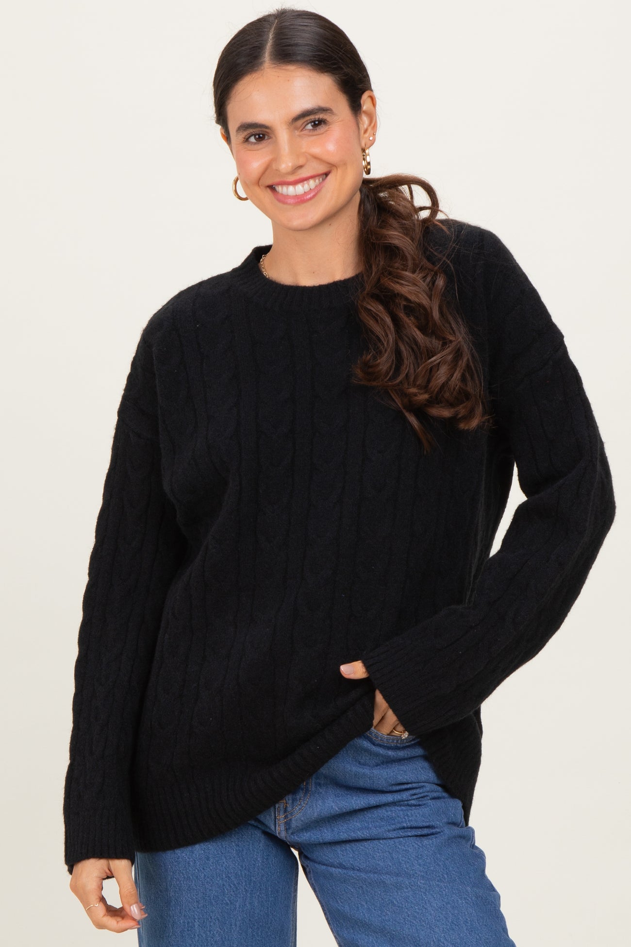 woman wearing a black cable knit sweater with long sleeves and a relaxed fit, smiling with one hand in her pocket