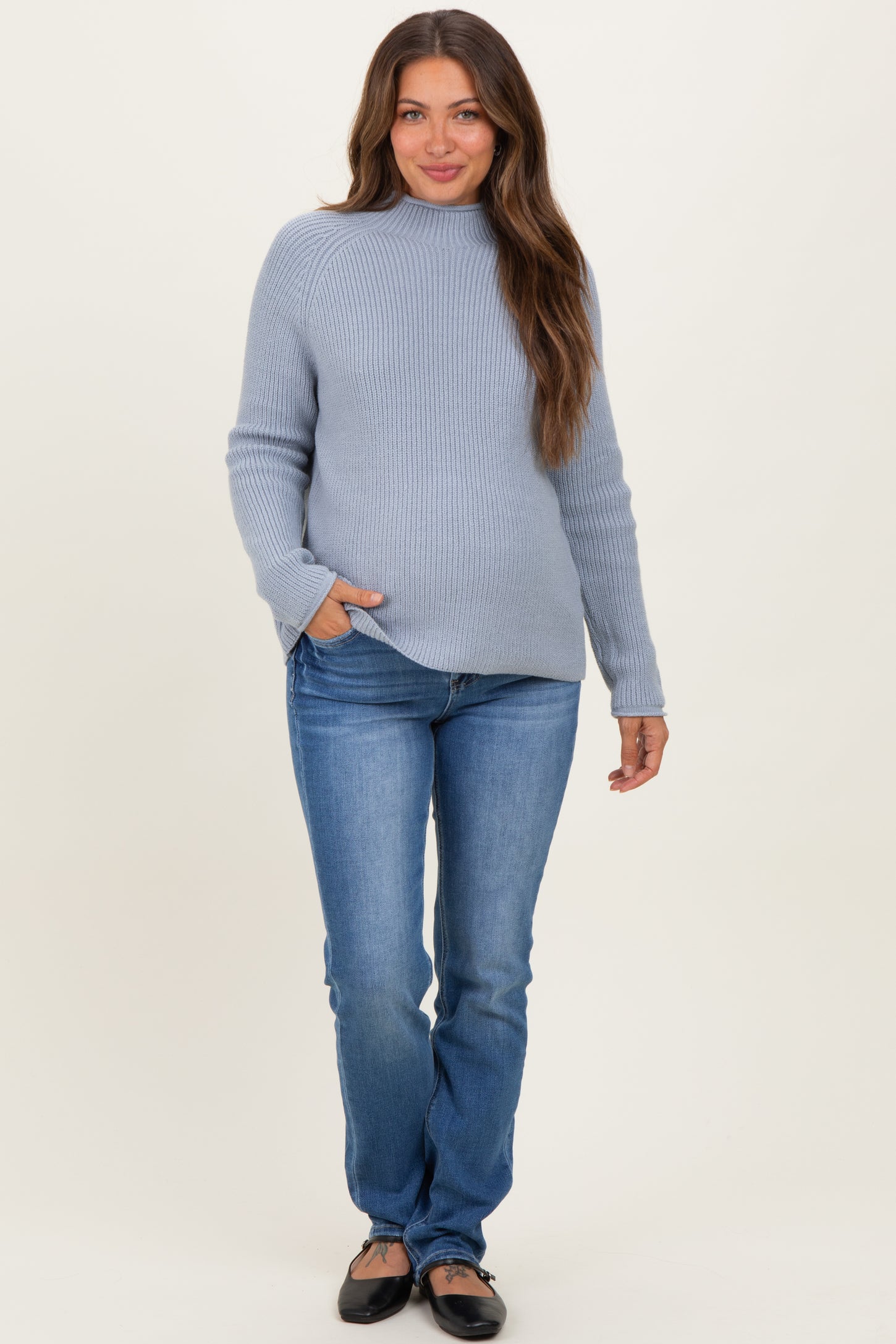 woman wearing a light blue maternity sweater and fitted jeans with a visible baby bump