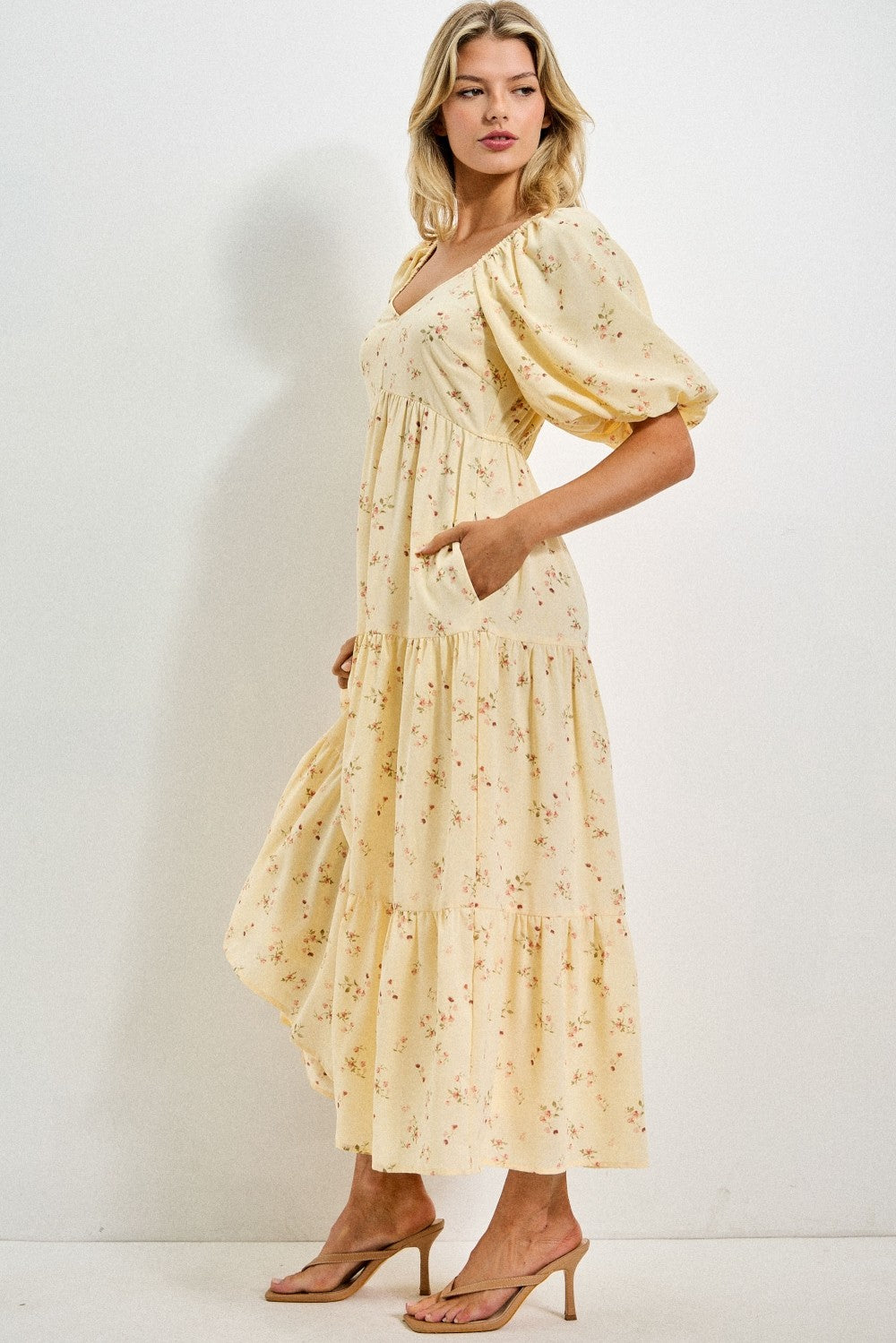 woman wearing a light yellow floral maxi dress with puff sleeves and pockets, standing in profile