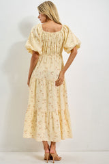 woman wearing a yellow floral maxi dress with puff sleeves and a tiered skirt, showing the back view