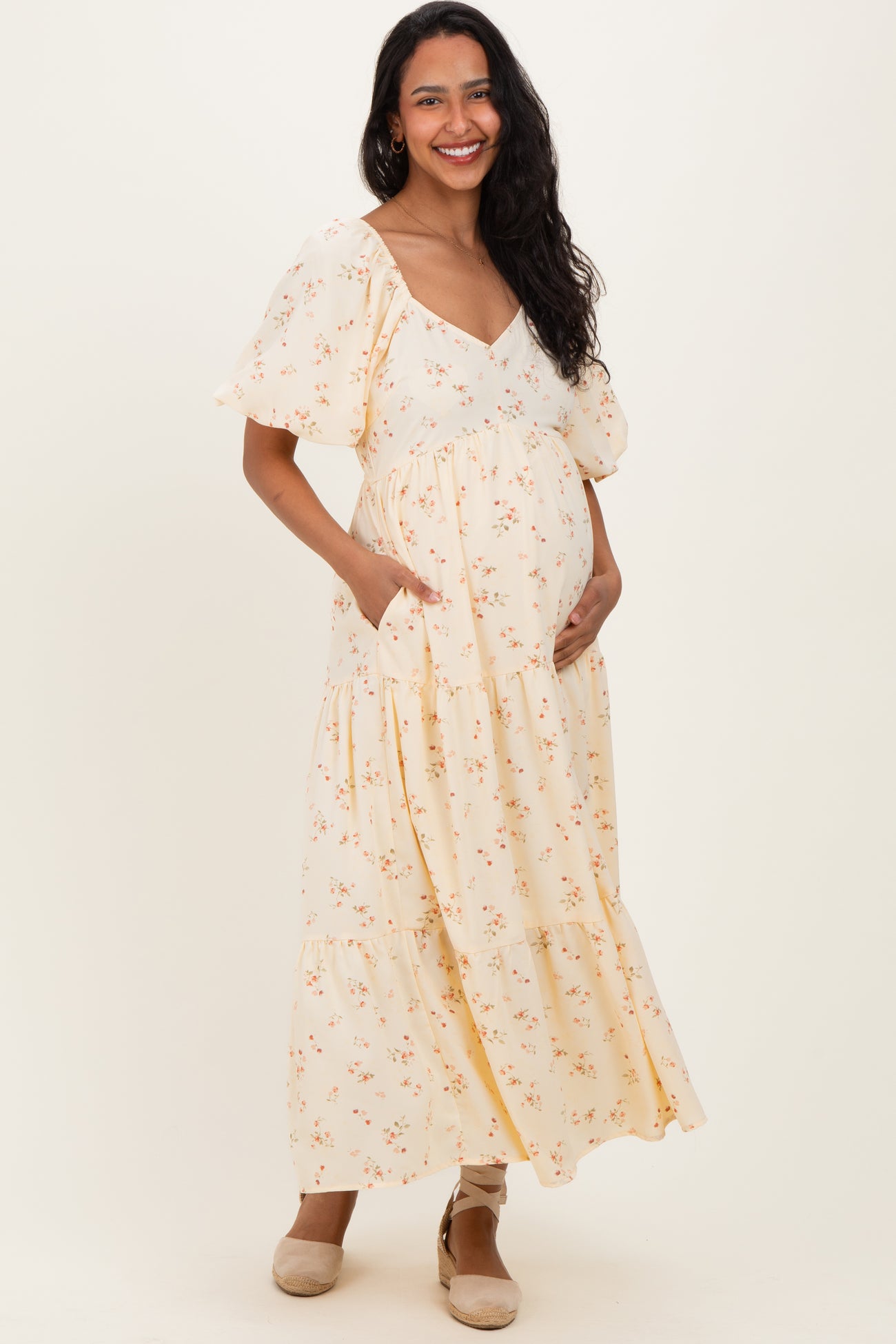 woman wearing a yellow floral maternity maxi dress with short puff sleeves and side pockets, showing her baby bump