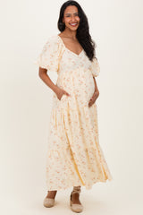 woman wearing a yellow floral maternity maxi dress with short puff sleeves and side pockets, showing her baby bump