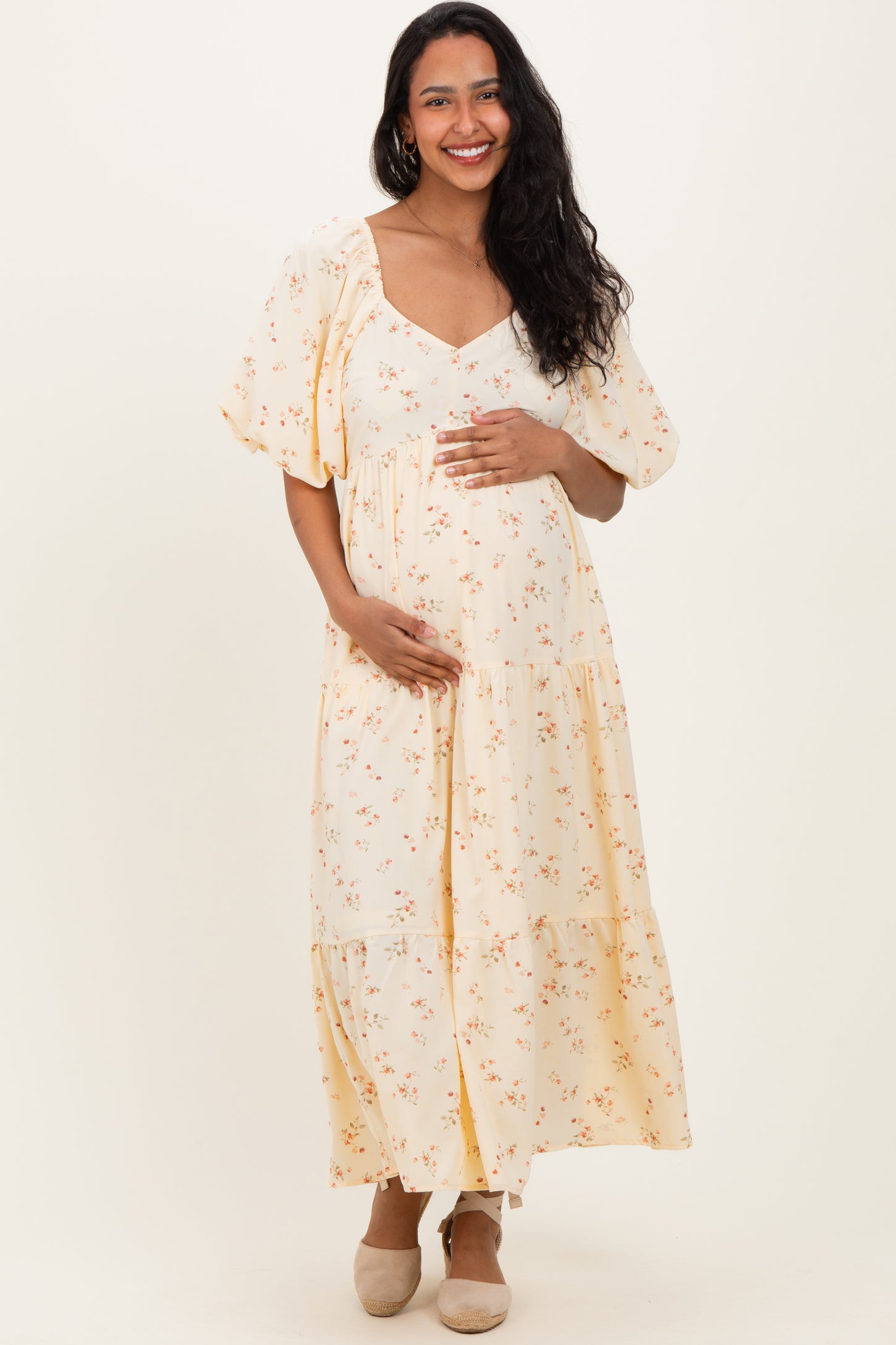 woman wearing a cream floral maternity maxi dress and holding her baby bump