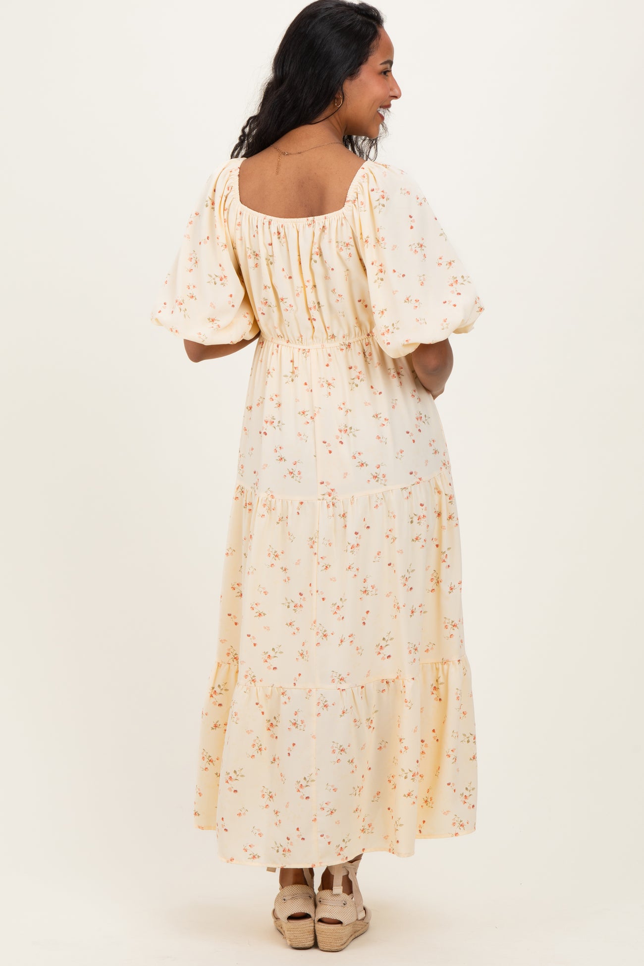 woman wearing a yellow floral patterned maternity maxi dress with puff sleeves and tiered skirt, showing her back