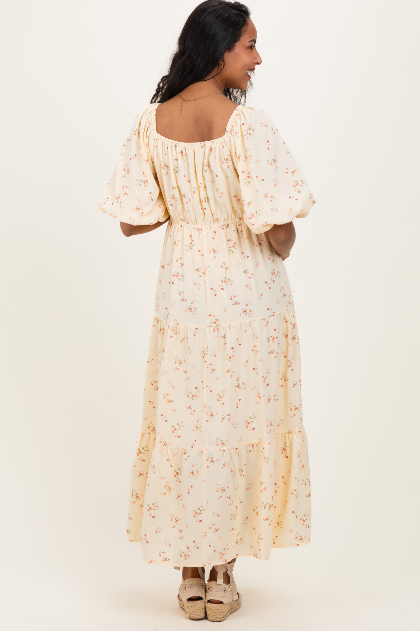 woman wearing a yellow floral patterned maternity maxi dress with puff sleeves and tiered skirt, showing her back