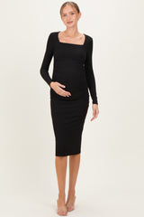 woman wearing a black long sleeve maternity dress with a square neckline and holding her baby bump