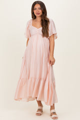 woman wearing a light pink maternity maxi dress with flutter sleeves and a gathered bodice, showing her baby bump