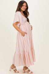 woman wearing a light pink maternity maxi dress with short sleeves and pockets, showcasing her baby bump