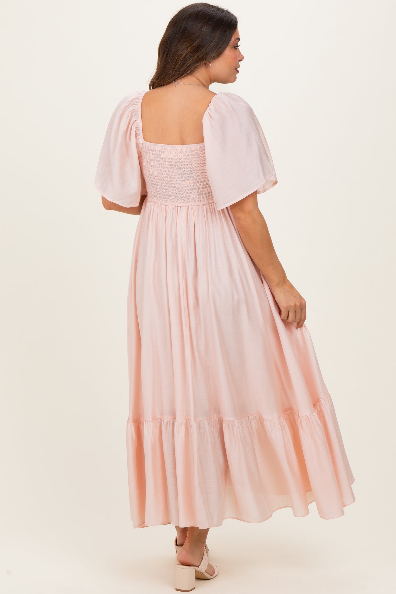 woman wearing a light pink maternity dress with a smocked bodice and puff sleeves, seen from the back