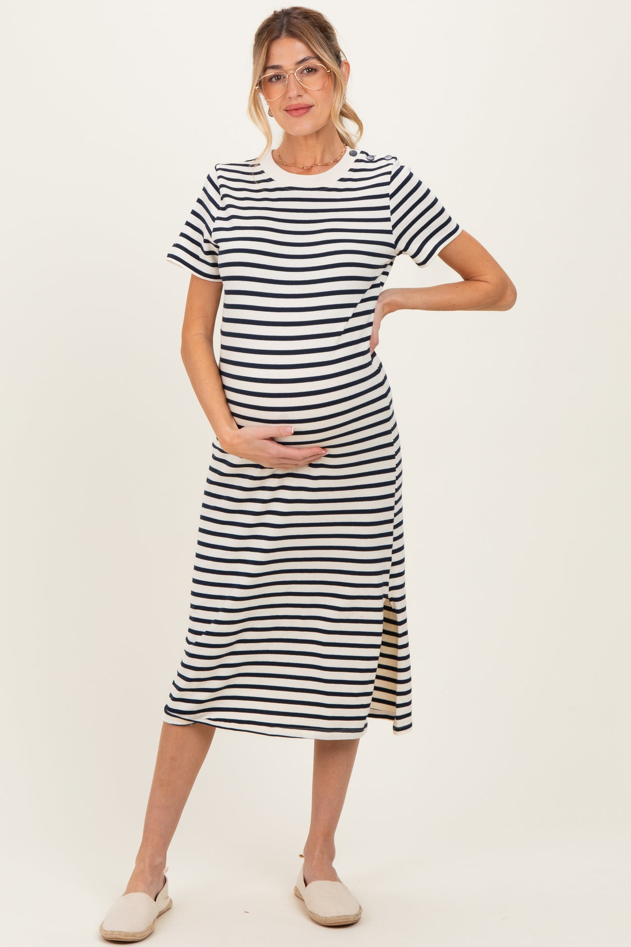 woman wearing a navy and white striped maternity dress with a side slit and holding her baby bump